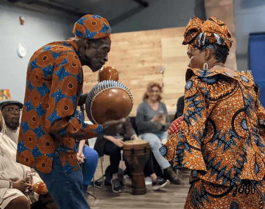 Percussionists in patterned attire performing with a shekere and drum during Therapeutic Percussion