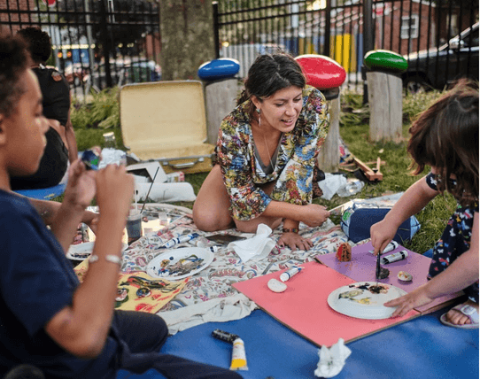A teaching artist and children painting outdoors during Visual Arts Studio